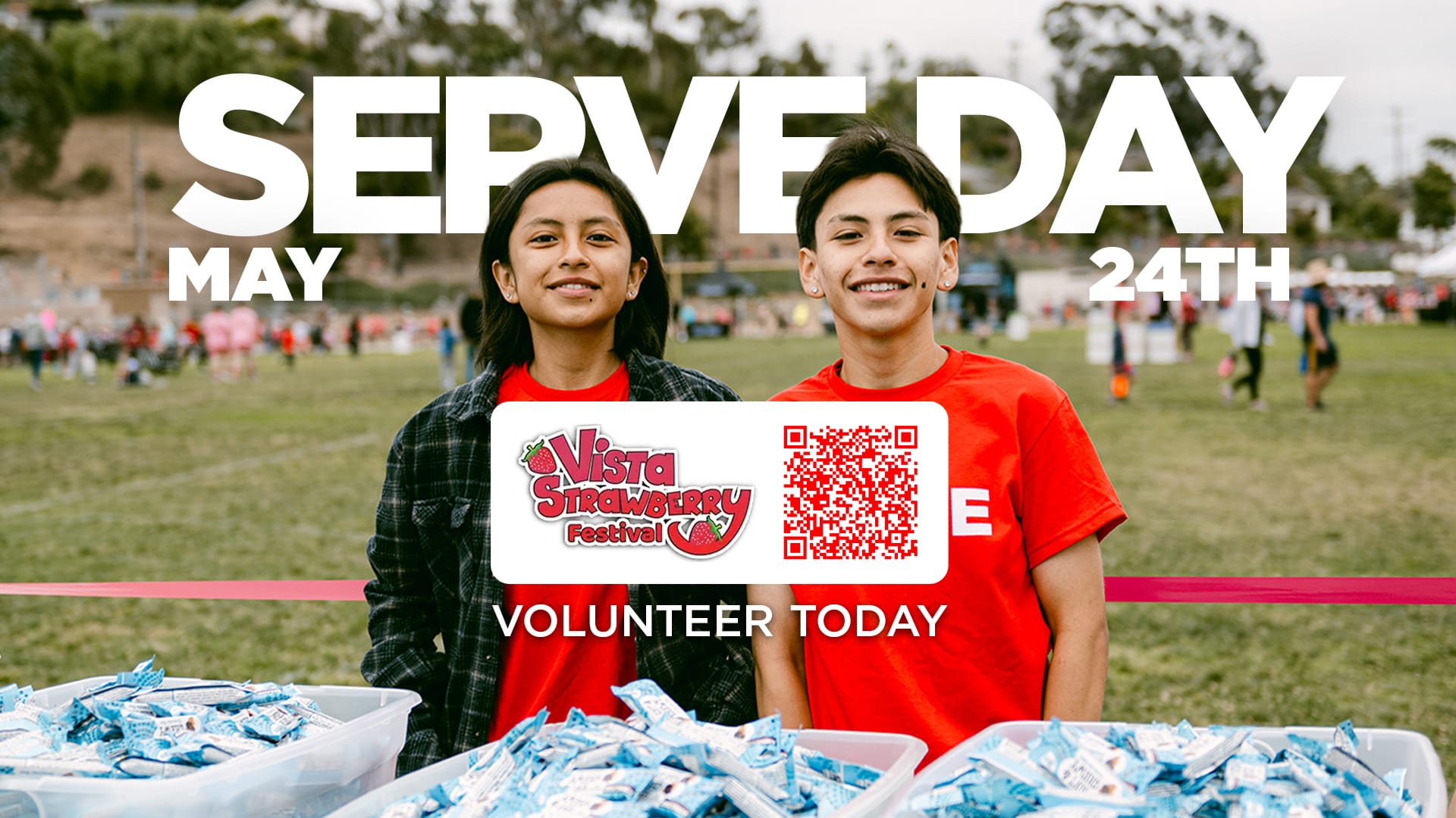 Two smiling volunteers in red shirts stand behind bins of packaged snacks at an outdoor event, with large text reading “Serve Day – May 24th” and a call to “Volunteer Today” alongside a Vista Strawberry Festival logo and QR code.