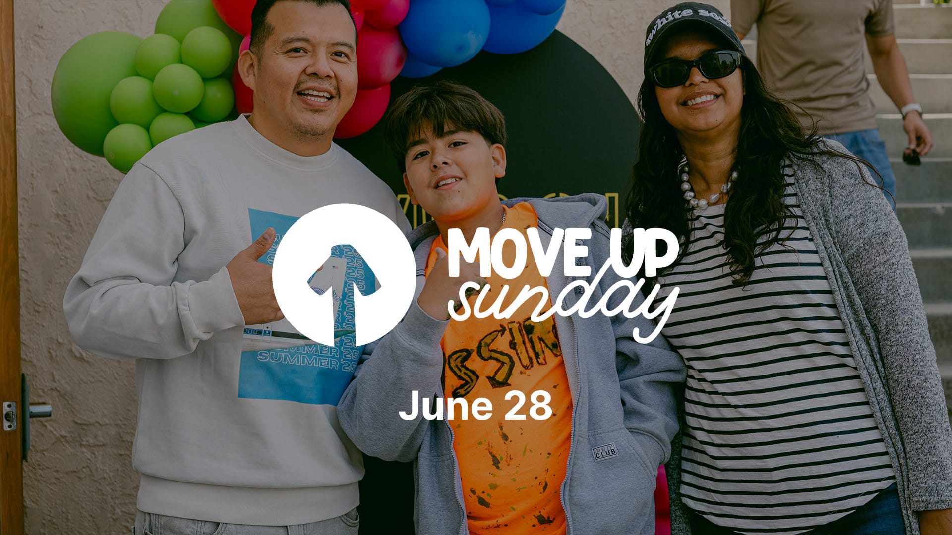 Family event graphic featuring three smiling people posing together in front of colorful balloons. White text reads ‘Move Up Sunday’ with an upward arrow icon and the date ‘June 28’ below. The group stands outdoors in casual clothing, celebrating a church kids ministry promotion event.